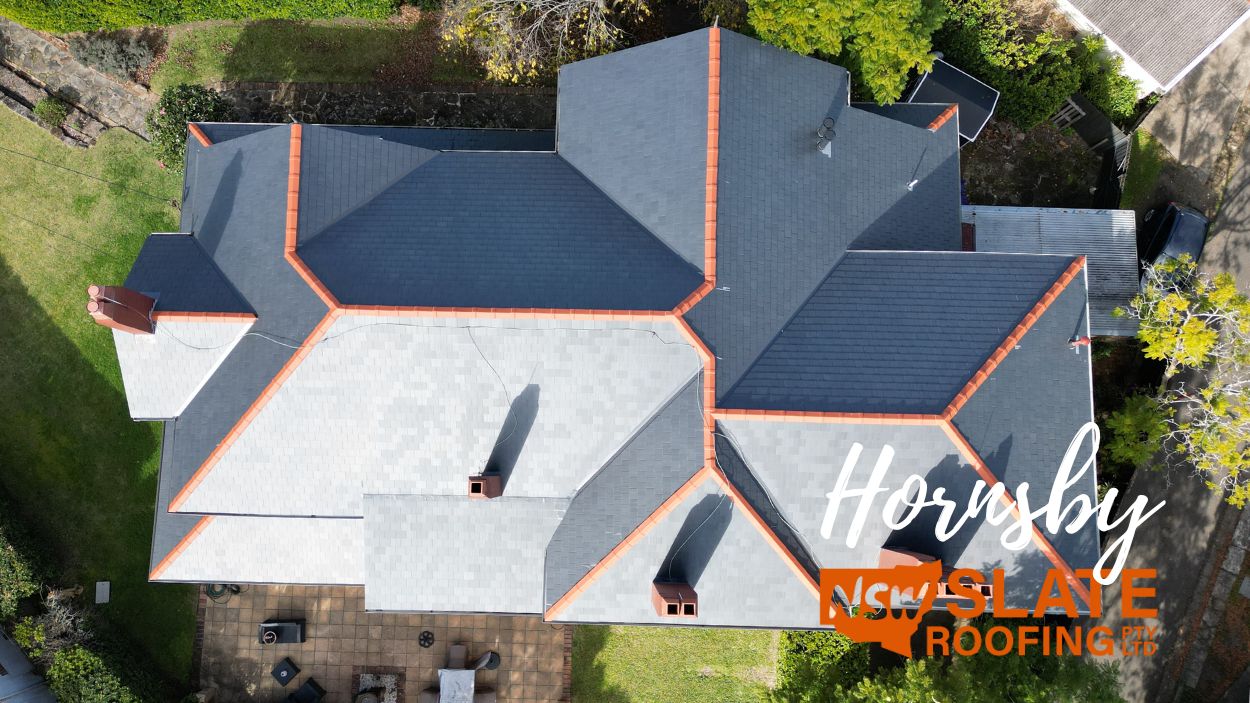Aerial view of a house with grey slate roof and orange trim, greenery, and patio. Hornsby New Slate Roofing Pty Ltd.