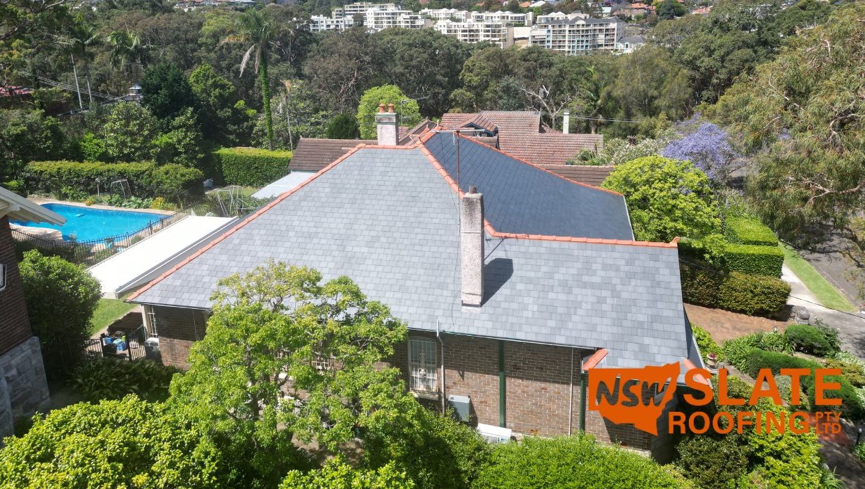 Slate Roofing Sydney Slate Roofing Manly Northern Beaches NSW Slate Roofing Sydney Aerial view of house with premium grey slate roof, brick walls, pool, and NSW Slate Roofing logo visible.